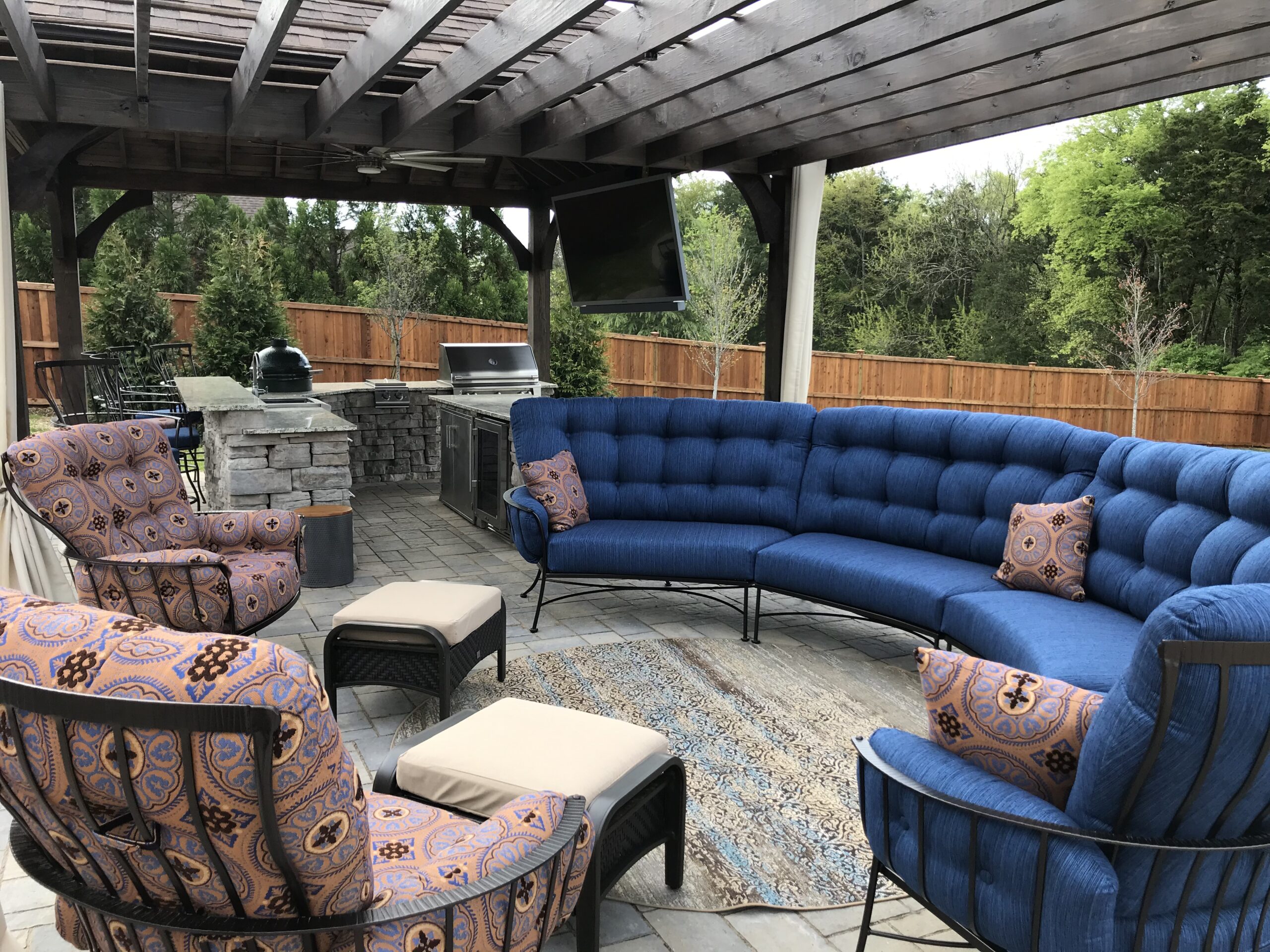 Custom outdoor living space in Nashville featuring a stone outdoor kitchen, built-in grill, and large blue sectional sofa under a dark wood pavilion.