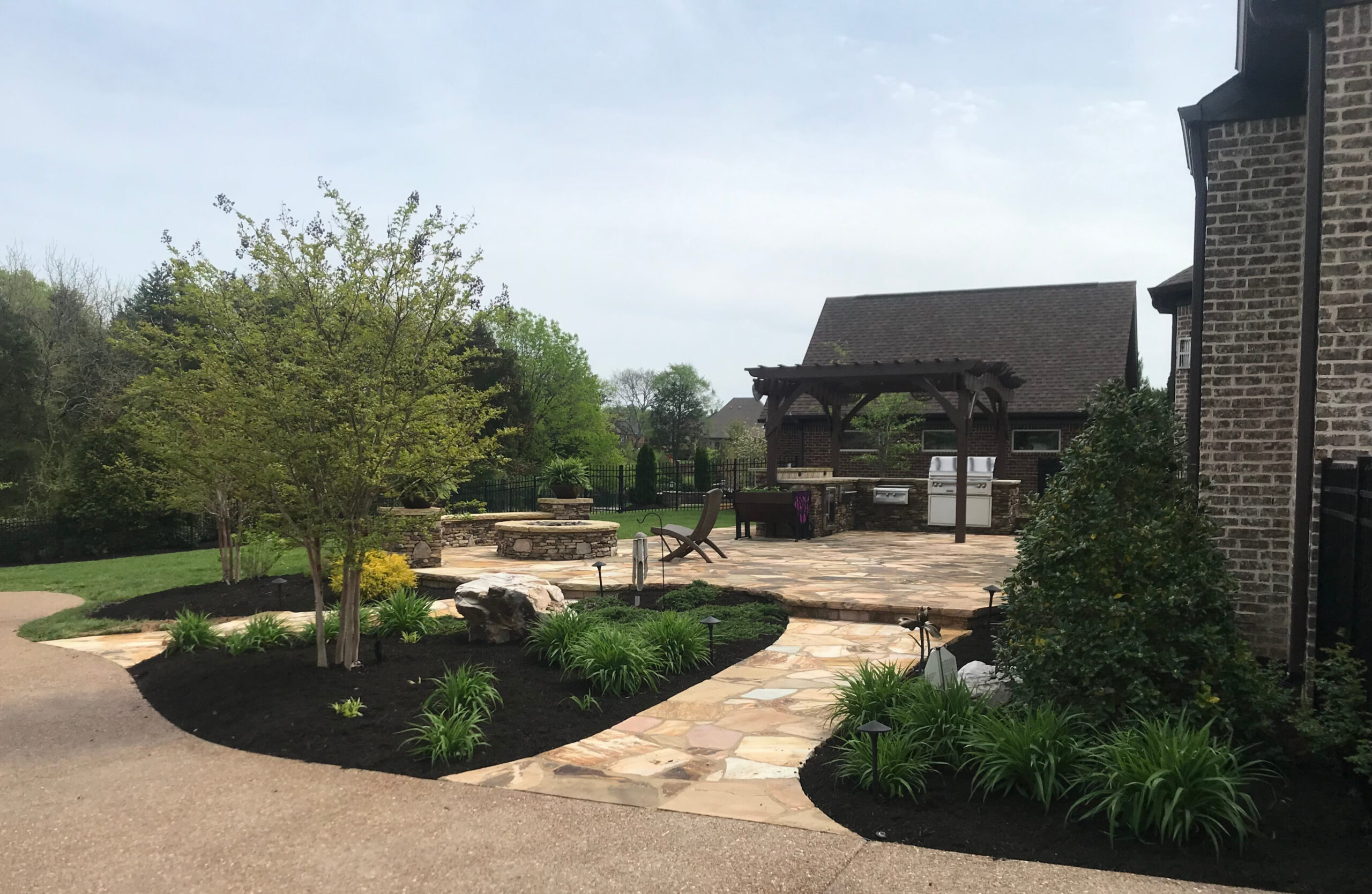 Custom flagstone patio with built-in stone fire pit, pergola-covered outdoor kitchen, and professionally landscaped planting beds at a Nashville-area residence
